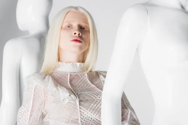 Young albino woman in trendy blouse looking at camera near mannequins on white background — Stock Photo