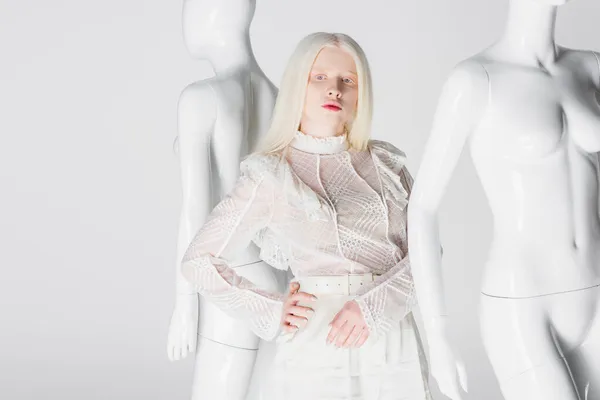 Молода альбіносова жінка в блузці тримає руку на стегні біля манекенів ізольовано на білому — стокове фото