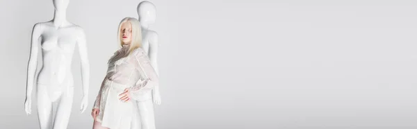 Albino woman in blouse standing with closed eyes near mannequins isolated on white, banner — Stock Photo