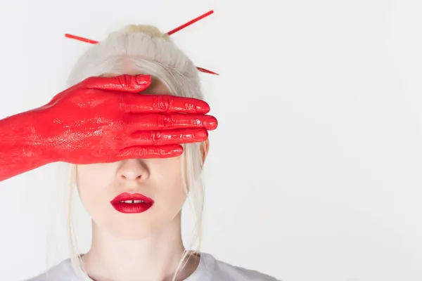 Mujer con pintura en la mano cubriendo la cara de modelo rubio con labios rojos aislados en blanco - foto de stock