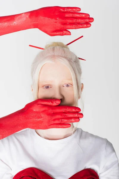Руки женщины в красной краске рядом со стильной моделью альбиноса, изолированной на белом — стоковое фото