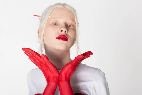 Young albino model with red lips looking at camera near female hands in paint isolated on white — Stock Photo