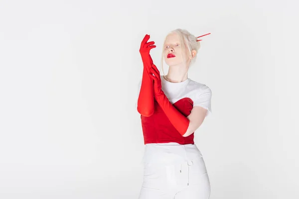 Mujer albina con estilo en guantes rojos mirando hacia otro lado aislado en blanco - foto de stock