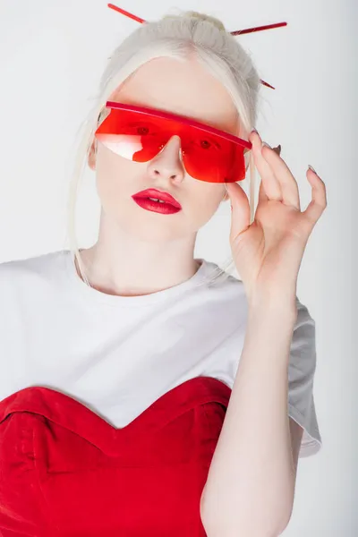 Mujer albina con estilo sosteniendo gafas de sol rojas aisladas en blanco - foto de stock