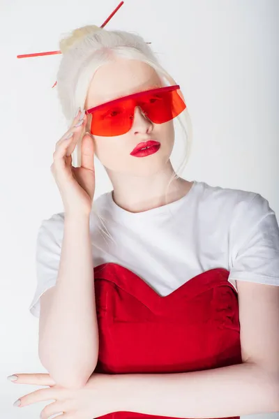 Elegante mujer rubia y albina en gafas de sol rojas posando aislada sobre blanco - foto de stock