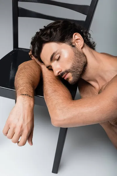 Uomo tatuato e senza camicia appoggiato su sedia in legno su grigio — Foto stock
