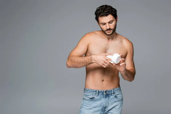 Contenitore uomo tatuato e senza camicia con crema cosmetica isolata su grigio — Foto stock