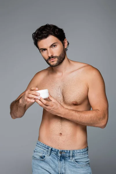 Shirtless man holding container with cosmetic cream isolated on grey — Stock Photo