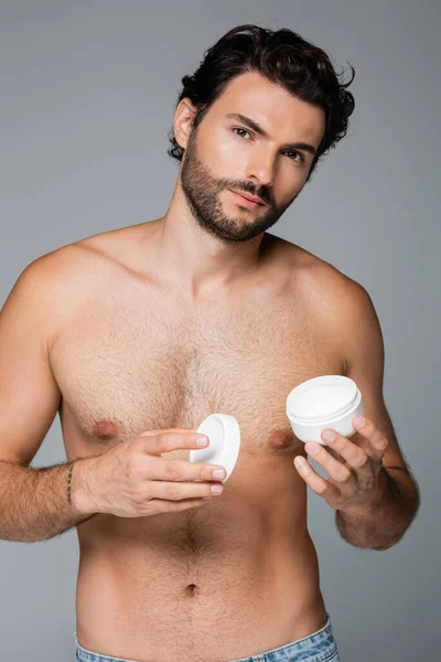 Tätowierter Mann hält Behälter mit Kosmetikcreme isoliert auf grau — Stockfoto