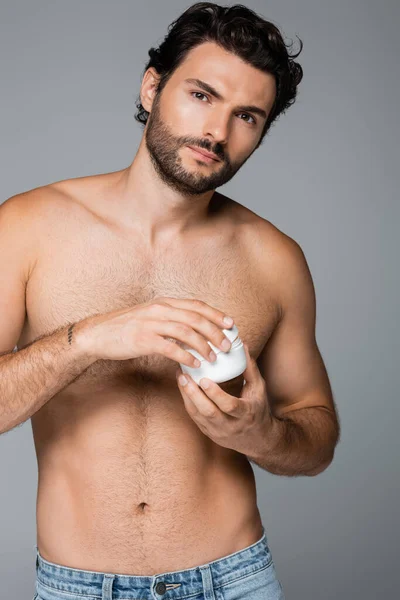 Homme tatoué et barbu tenant récipient avec crème cosmétique isolé sur gris — Photo de stock