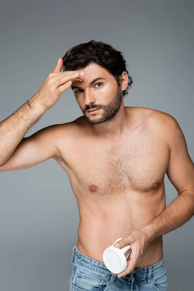 Hombre tatuado y sin camisa aplicando crema facial aislada en gris - foto de stock