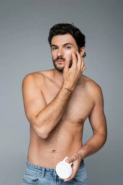 Giovane uomo senza camicia contenente contenitore con crema cosmetica isolata su grigio — Foto stock
