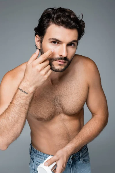 Hombre sin camisa aplicando crema facial aislada en gris - foto de stock