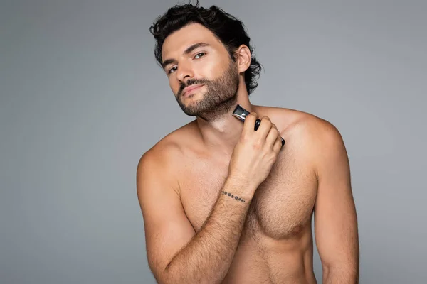 Young man trimming beard isolated on grey — Stock Photo