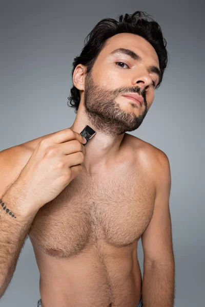 Tätowierter und hemdloser Mann schneidet Bart isoliert auf grau — Stockfoto