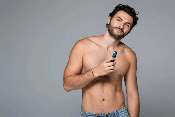 Joven hombre sin camisa sosteniendo afeitadora eléctrica aislado en gris - foto de stock