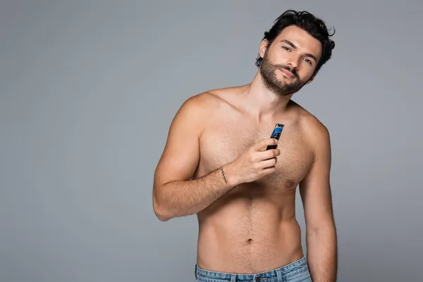 Giovane uomo senza camicia che tiene rasoio elettrico isolato su grigio — Foto stock