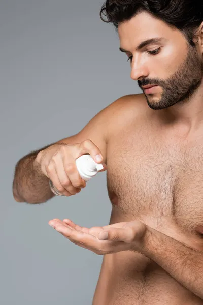 Hombre barbudo y sin camisa sosteniendo limpiador de espuma aislado en gris - foto de stock