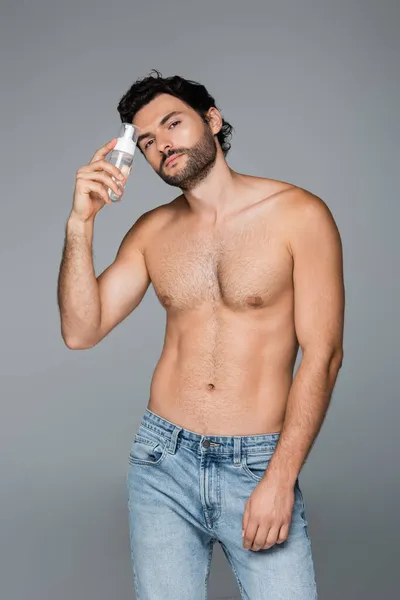 Shirtless man in jeans holding foam cleanser isolated on grey — Stock Photo