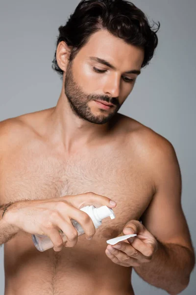 Hombre sin camisa aplicando tóner sobre almohadilla de algodón aislado en gris - foto de stock