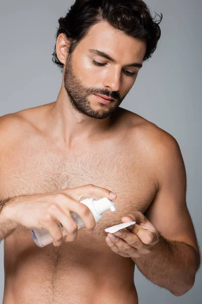 Uomo barbuto e senza camicia che applica toner sul batuffolo di cotone isolato su grigio — Foto stock