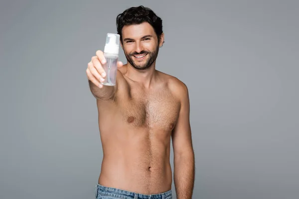 Uomo gioioso e senza camicia che tiene detergente in schiuma isolato su grigio — Foto stock