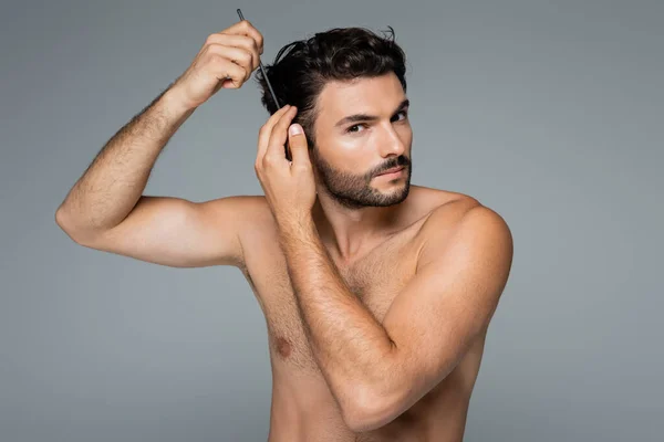 Fokussierte hemdlose Mann Bürsten welliges Haar mit Kamm isoliert auf grau — Stockfoto