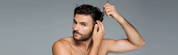 Shirtless man brushing wavy hair with comb isolated on grey, banner — Stock Photo