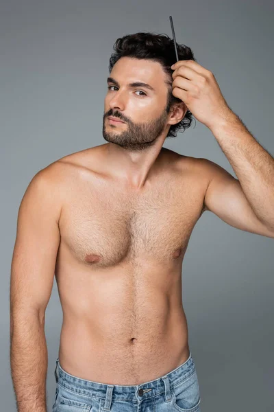 Hombre sin camisa cepillado pelo ondulado con peine aislado en gris - foto de stock