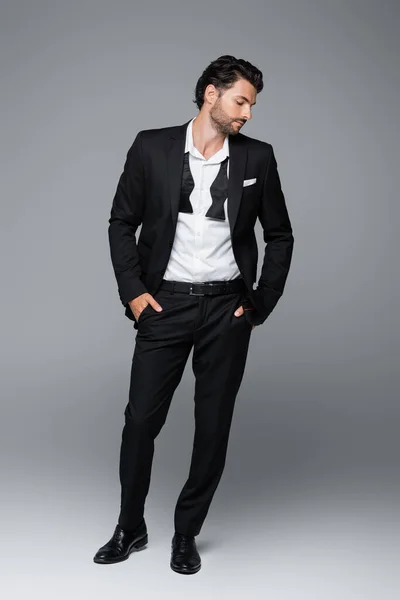 Full length of bearded model in suit posing with hands in pockets on grey — Stock Photo