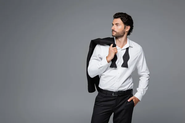 Hombre barbudo en traje que sostiene la chaqueta y de pie con la mano en el bolsillo aislado en gris — Stock Photo