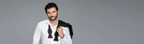 Hombre barbudo de traje sosteniendo la chaqueta mientras mira la cámara aislada en gris, pancarta - foto de stock