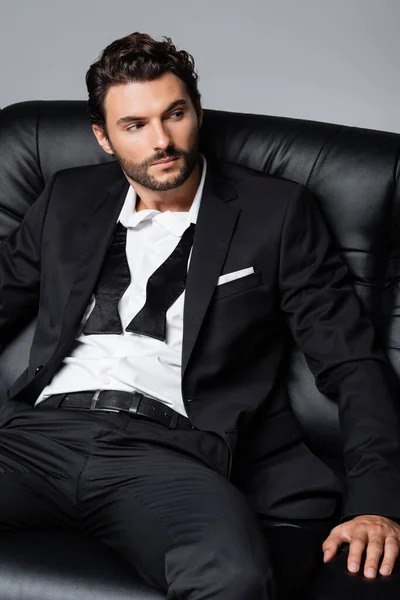 Bearded man in formal wear sitting on black couch isolated on grey — Stock Photo