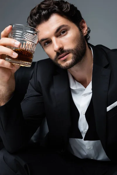 Hombre barbudo en desgaste formal sosteniendo vaso de whisky aislado en gris - foto de stock