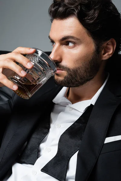 Bärtiger Mann mit welligem Haar trinkt Brandy isoliert auf grau — Stockfoto