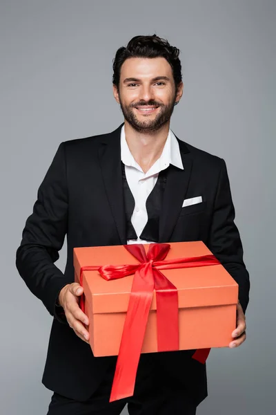 Homme heureux en costume tenant boîte rouge isolé sur gris — Photo de stock