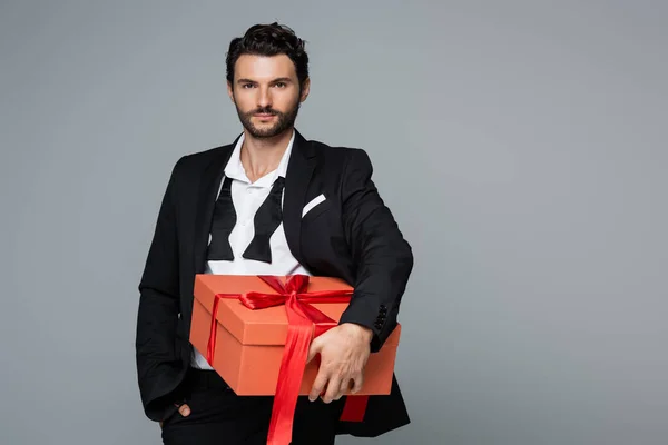 Young bearded man in suit holding red present isolated on grey — Stock Photo