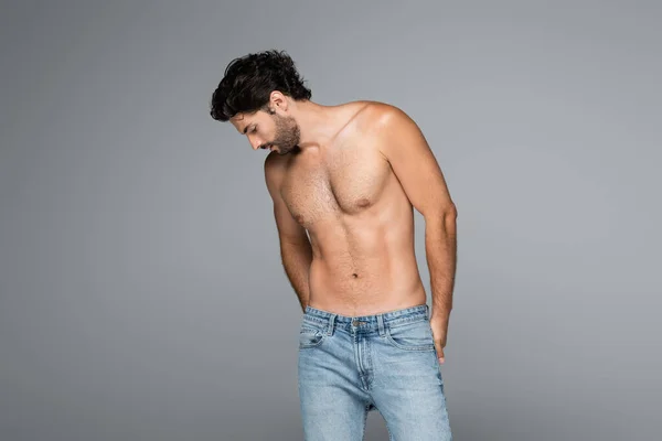 Bello e muscoloso uomo in blue jeans guardando giù isolato sul grigio — Foto stock