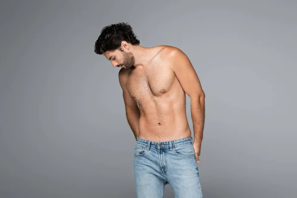 Homem bonito e musculoso em jeans azul olhando para baixo isolado em cinza — Stock Photo