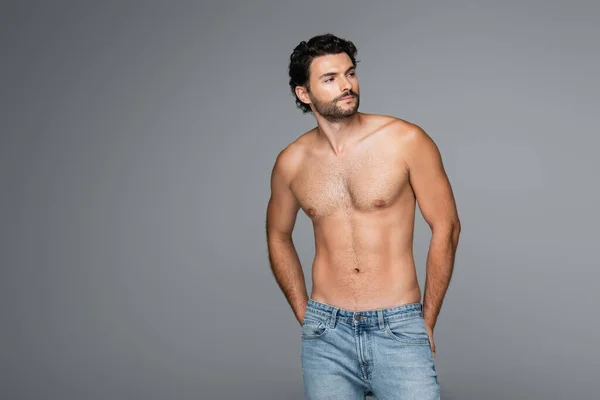 Homem bonito e musculoso em jeans olhando awat isolado em cinza — Fotografia de Stock
