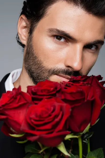 Primer plano del hombre barbudo sosteniendo ramo de rosas rojas aisladas en gris - foto de stock