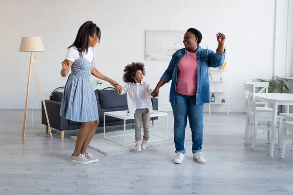 Щаслива афроамериканська дівчинка-малюк тримає руки з мамою і бабусею під час танців вдома — стокове фото