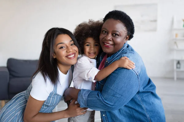 Mulheres americanas africanas alegres olhando para a câmera enquanto abraça a menina criança — Fotografia de Stock