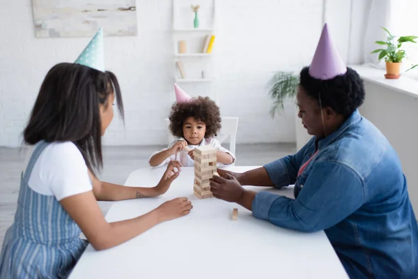 Afrikanisch-amerikanische Frauen und Kind in Party-Mützen spielen Holzklötze Spiel zu Hause — Stockfoto