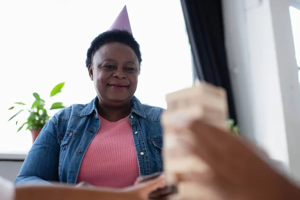 Happy african american middle aged woman looking at blurred family playing wood blocks game — Stock Photo