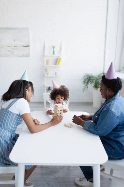 Mulheres africanas americanas e menina criança em bonés de festa jogando blocos de madeira jogo em casa — Fotografia de Stock