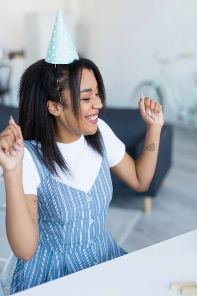 Eccitata donna afroamericana in berretto da festa sorridente con gli occhi chiusi a casa — Foto stock