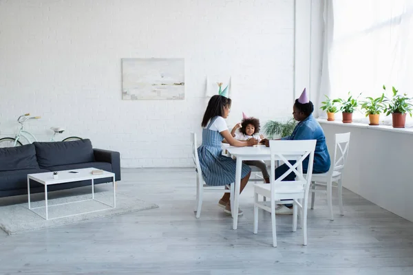 African american women and girl in party caps playing wood blocks game in spacious living room — Stock Photo
