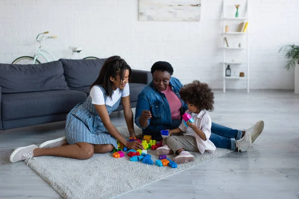 Mulheres africanas americanas jogando blocos de construção jogo com a menina criança no chão em casa — Fotografia de Stock