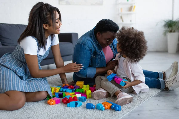 Femmes afro-américaines d'âge moyen et jeunes jouant jeu de blocs de construction avec enfant sur le sol à la maison — Photo de stock